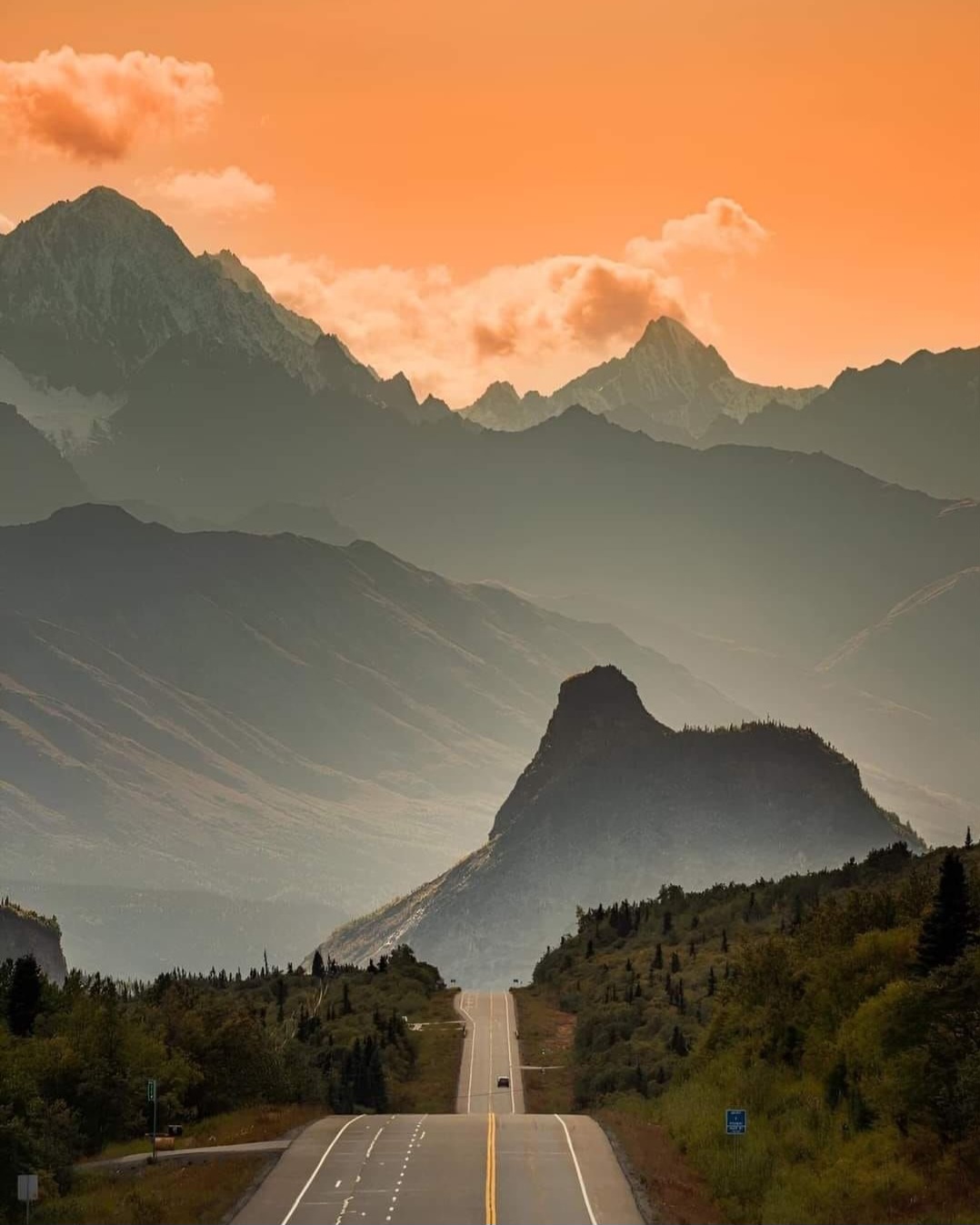 a view on a road in alaska with an orange sky. Probably during a sundown